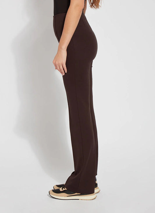 A side-profile view of a model wearing dark brown wide-leg pants and black sneakers with beige soles, set against a plain light gray studio background.