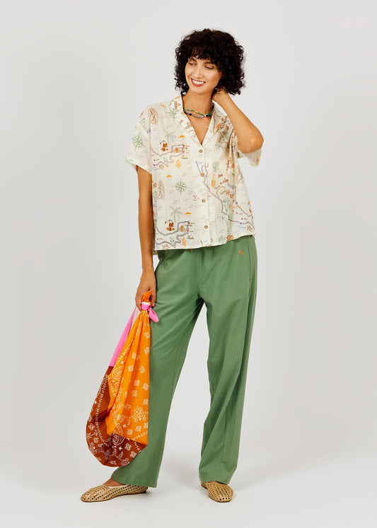 Woman wearing a patterned shirt and green pants, holding an orange bag on a white background