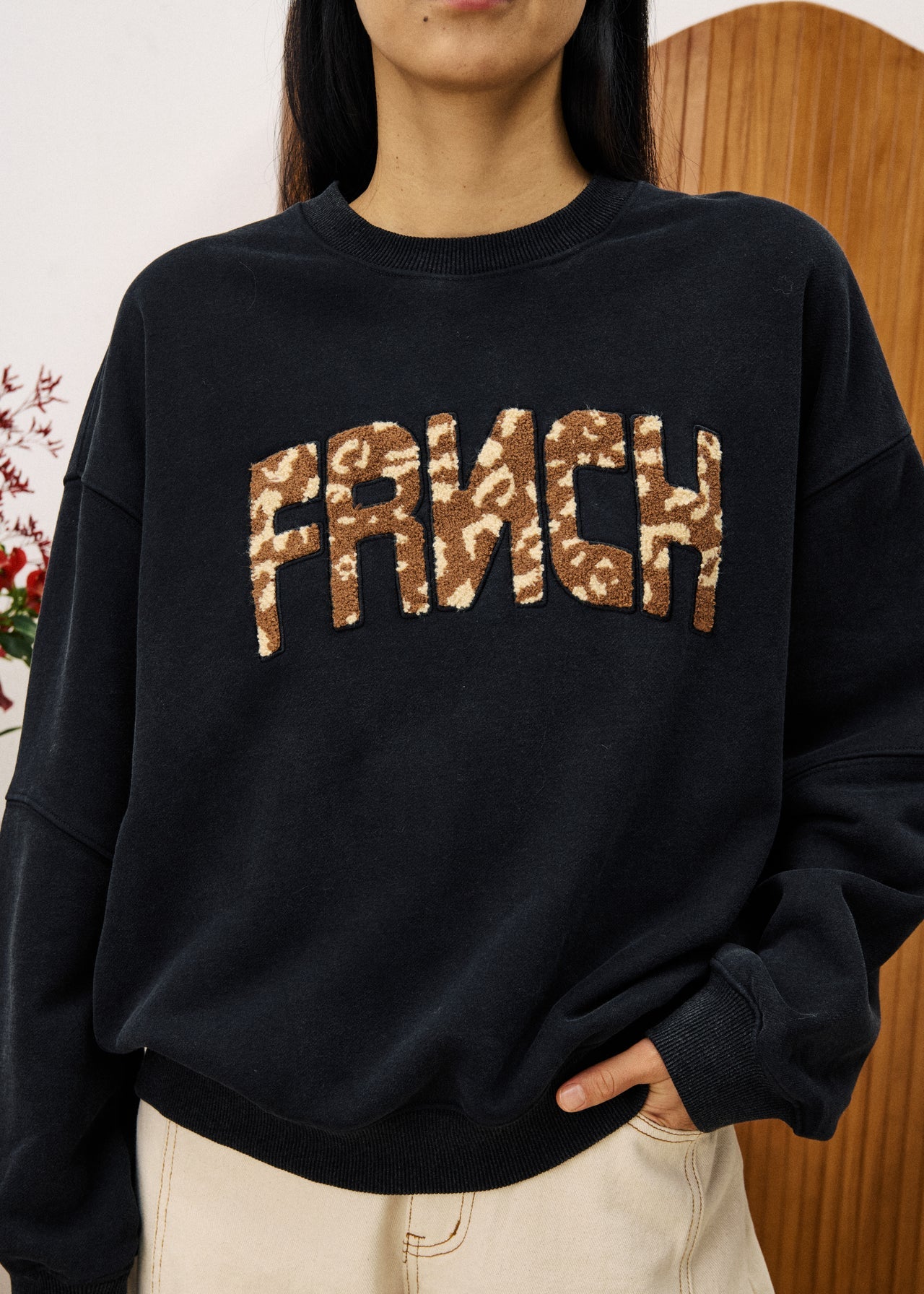 Person wearing a black sweatshirt with 'FRENCH' in leopard print letters.
