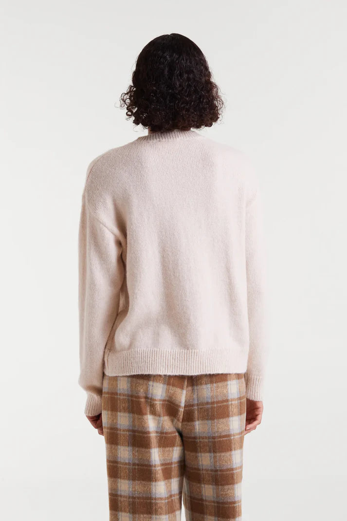 Person wearing a beige sweater and plaid pants on a white background