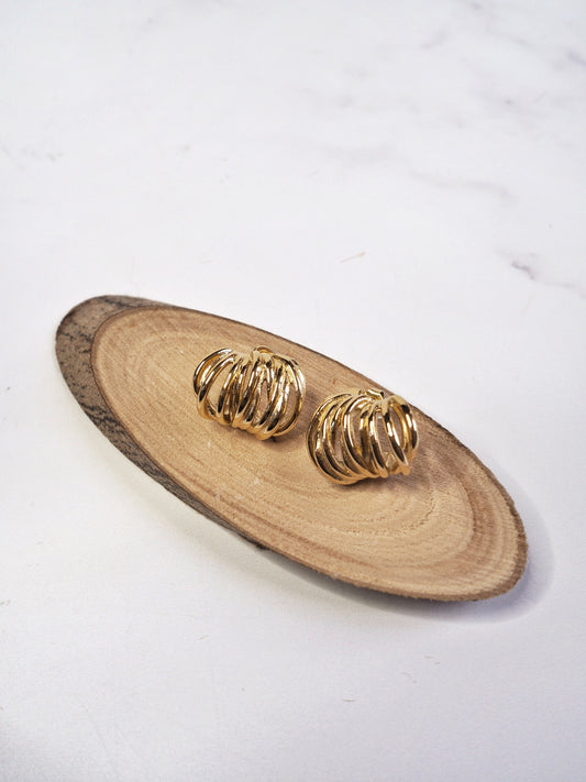 Gold earrings on a wooden tray with a white background