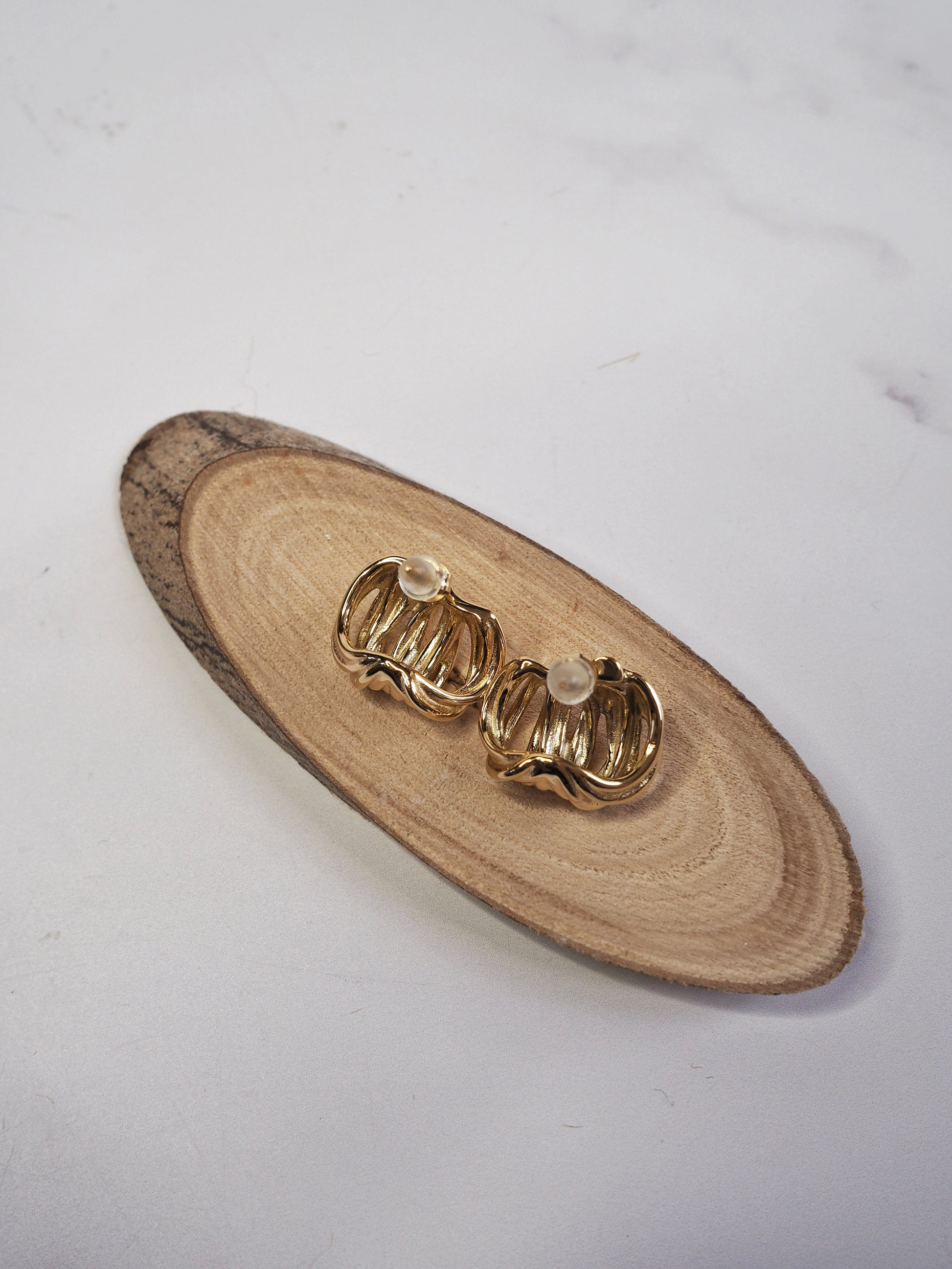 Gold earrings on a wooden tray with a white background