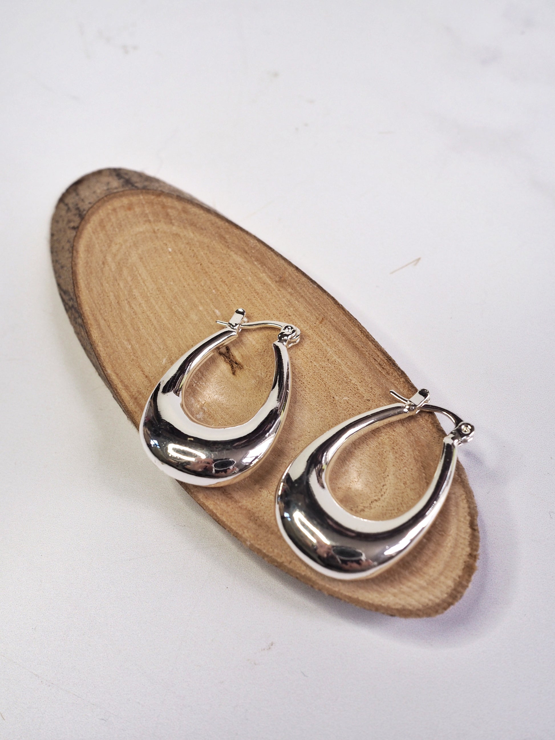Silver hoop earrings on a wooden stand with a white background