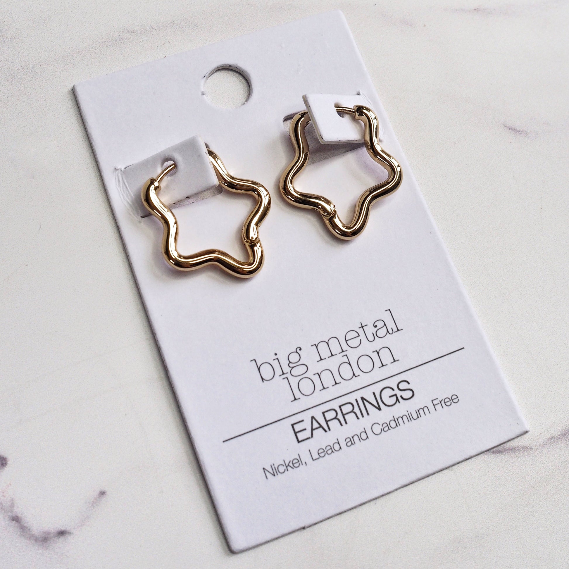 Gold star-shaped earrings on a 'big metal london' card against a marble background