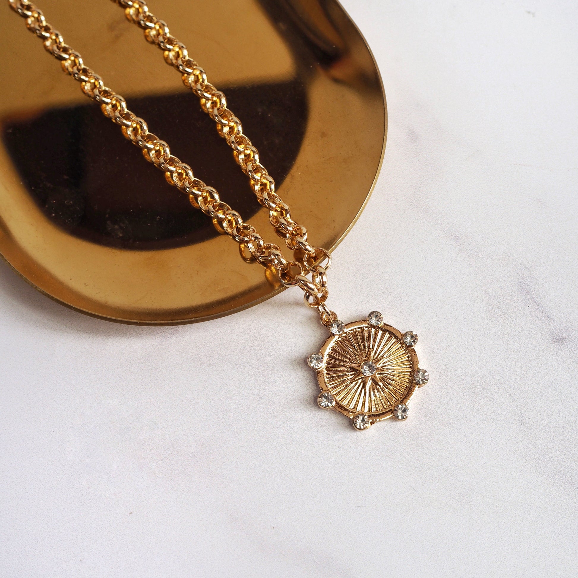 Gold necklace with a circular pendant on a white surface