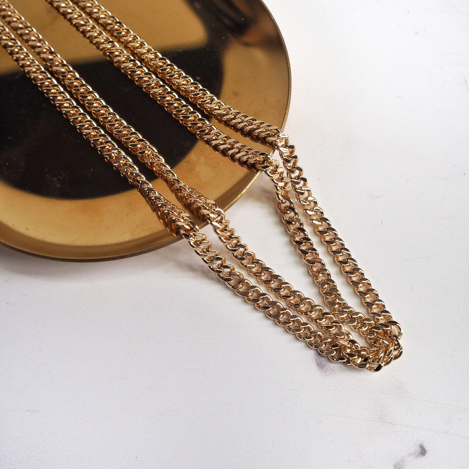 Gold chain necklace on a marble surface with a reflective background