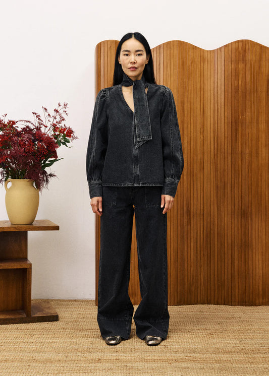 Person wearing a black denim outfit standing in front of a wooden screen with a vase of flowers on a table.