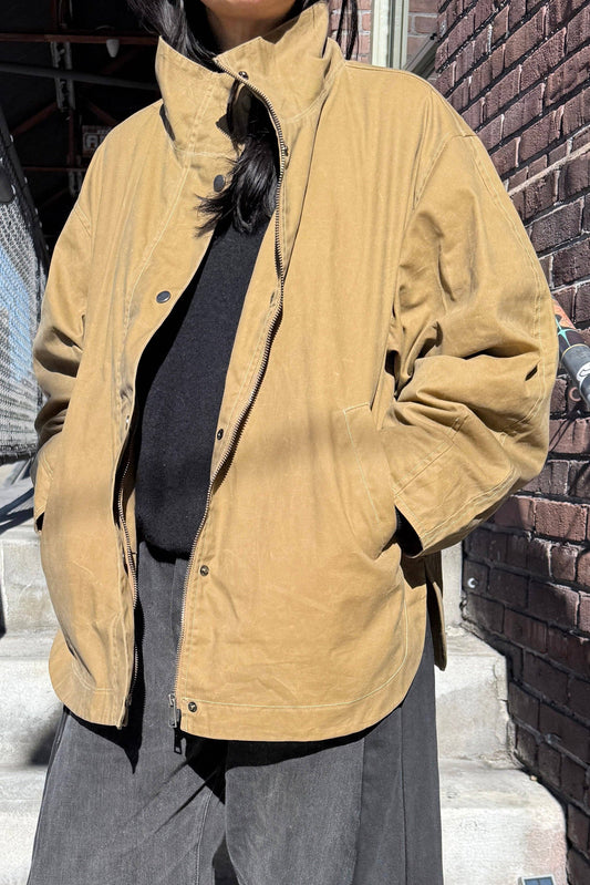 Person wearing a tan jacket standing against a brick wall.