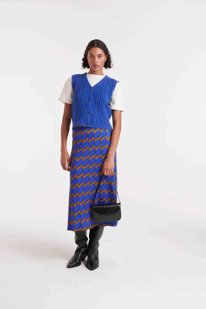 Woman wearing a blue patterned dress over a white shirt with a blue vest on a white background