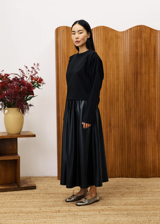 Woman in a black outfit standing in front of a wooden screen with a vase of flowers on a table.
