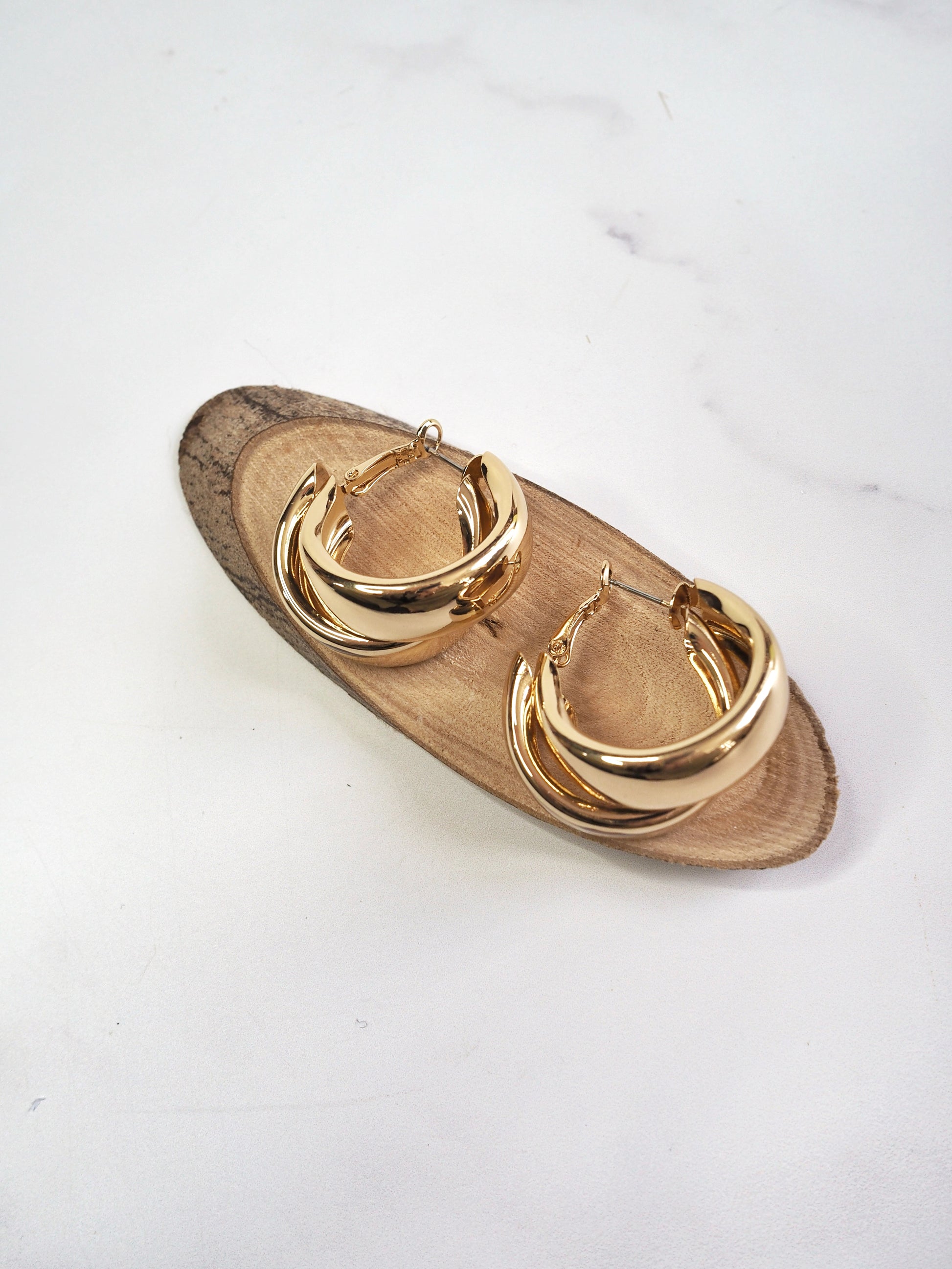 Gold hoop earrings on a wooden stand against a white background