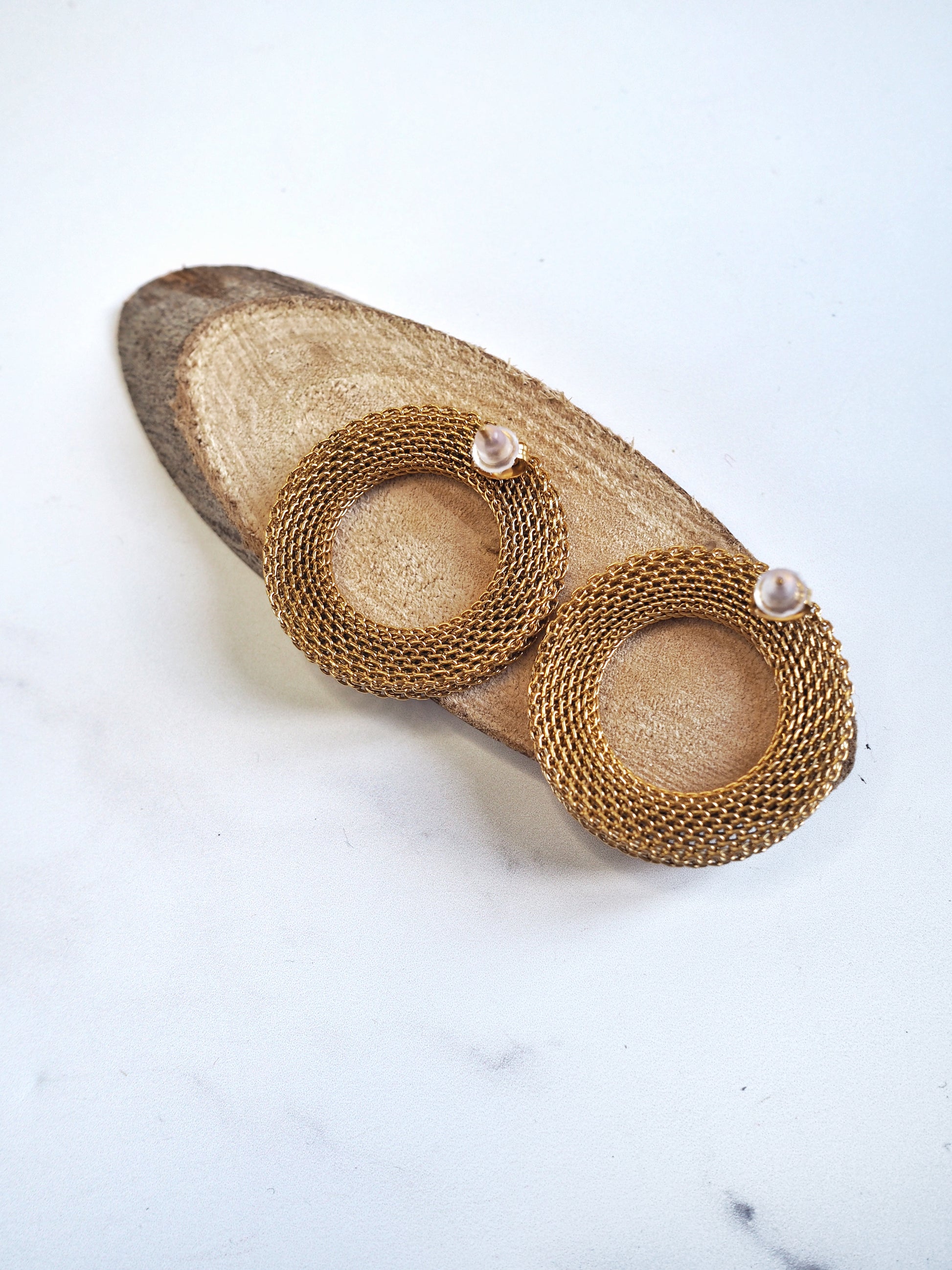 Gold mesh earrings on a white marble surface