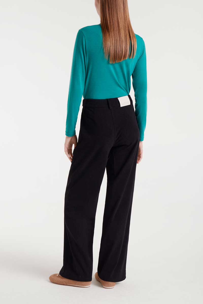 Person wearing a teal long-sleeve top and black pants on a white background