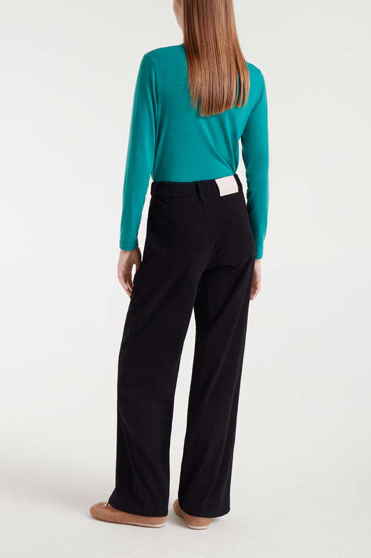 Person wearing a teal long-sleeve top and black pants on a white background