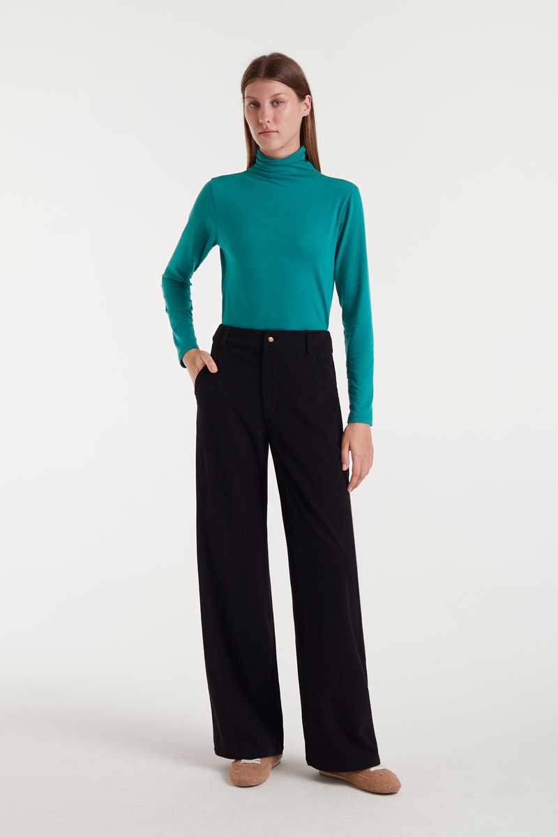 Woman wearing a teal turtleneck and black pants on a white background