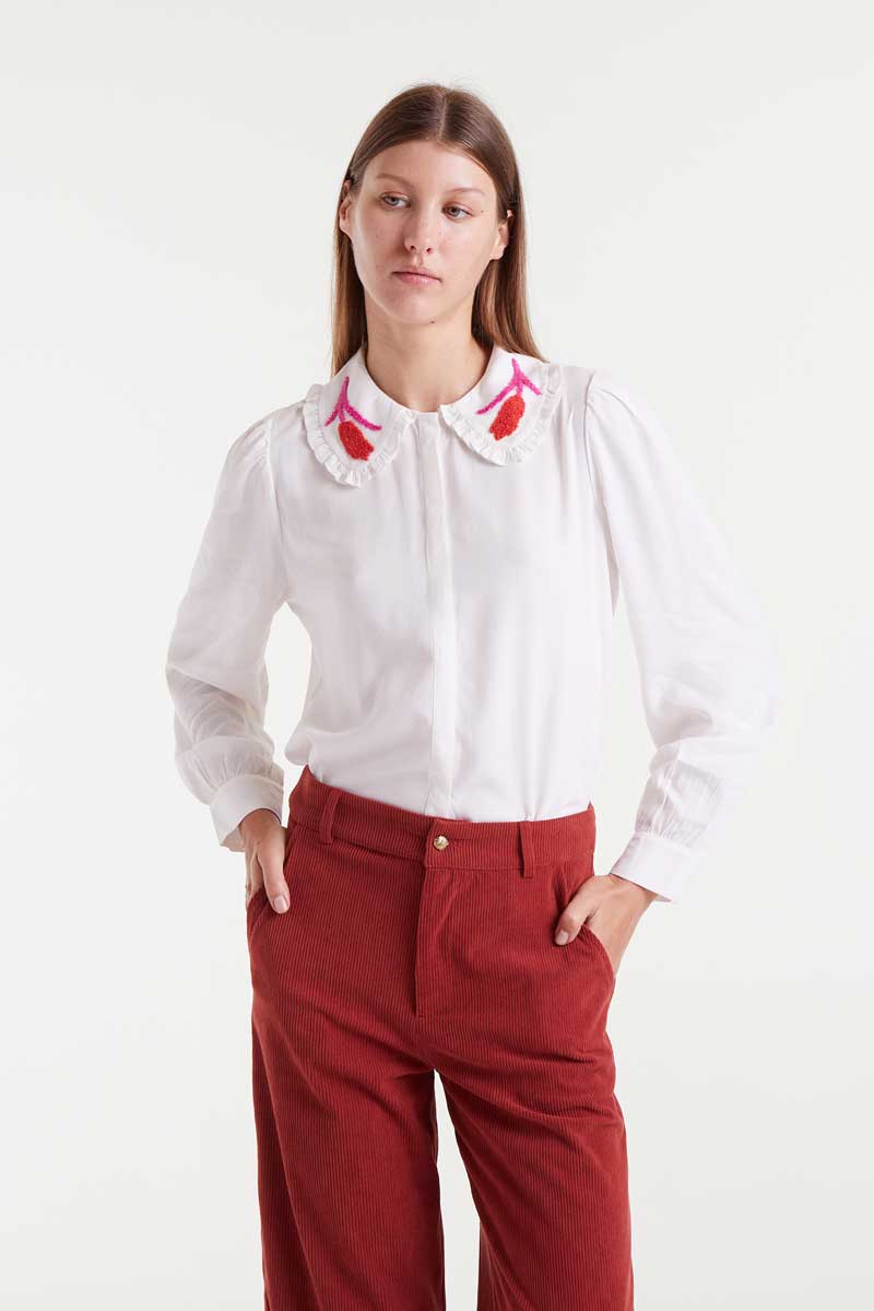 Woman wearing a white blouse with red floral embroidery and red pants on a white background
