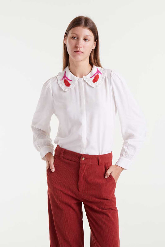 Woman wearing a white blouse with red floral embroidery and red pants on a white background