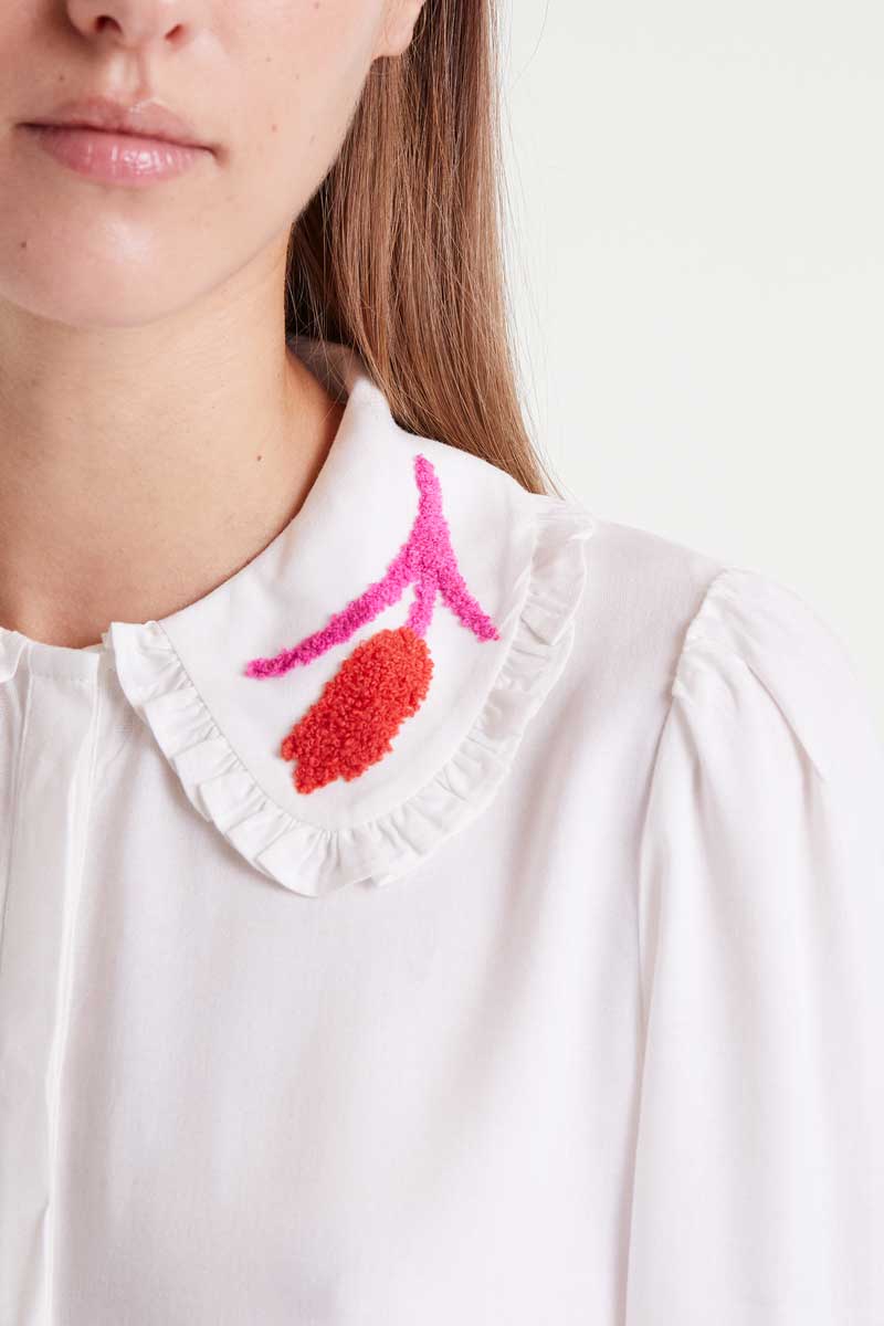 Close-up of a white shirt with a colorful embroidered collar against a white background