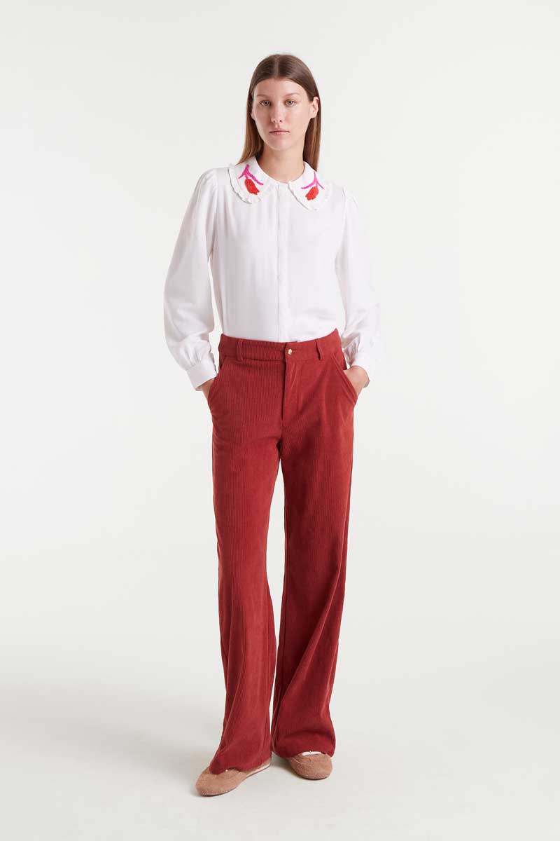 Woman wearing a white blouse with red accents and red pants on a white background