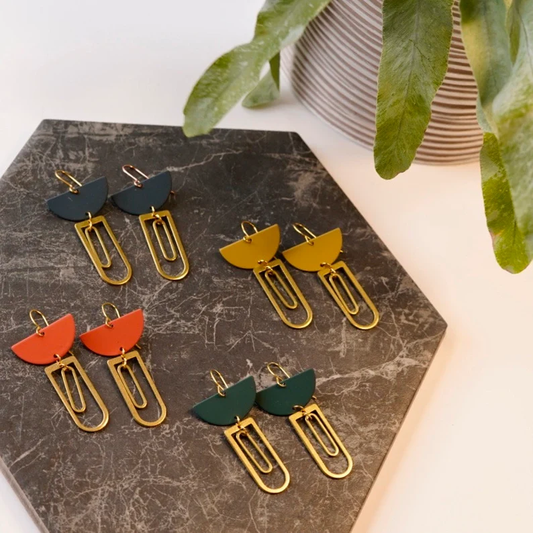 Pair of earrings on a marble surface with a plant in the background