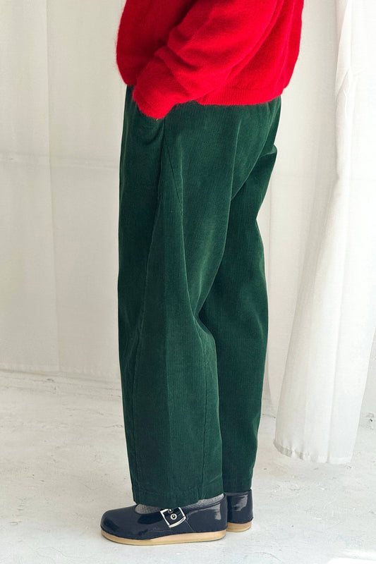 Person wearing green pants and a red top against a white curtain background