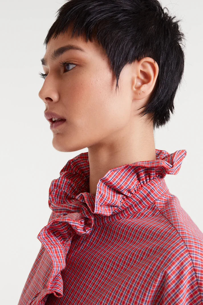 Person wearing a red checkered shirt with ruffled collar on a white background