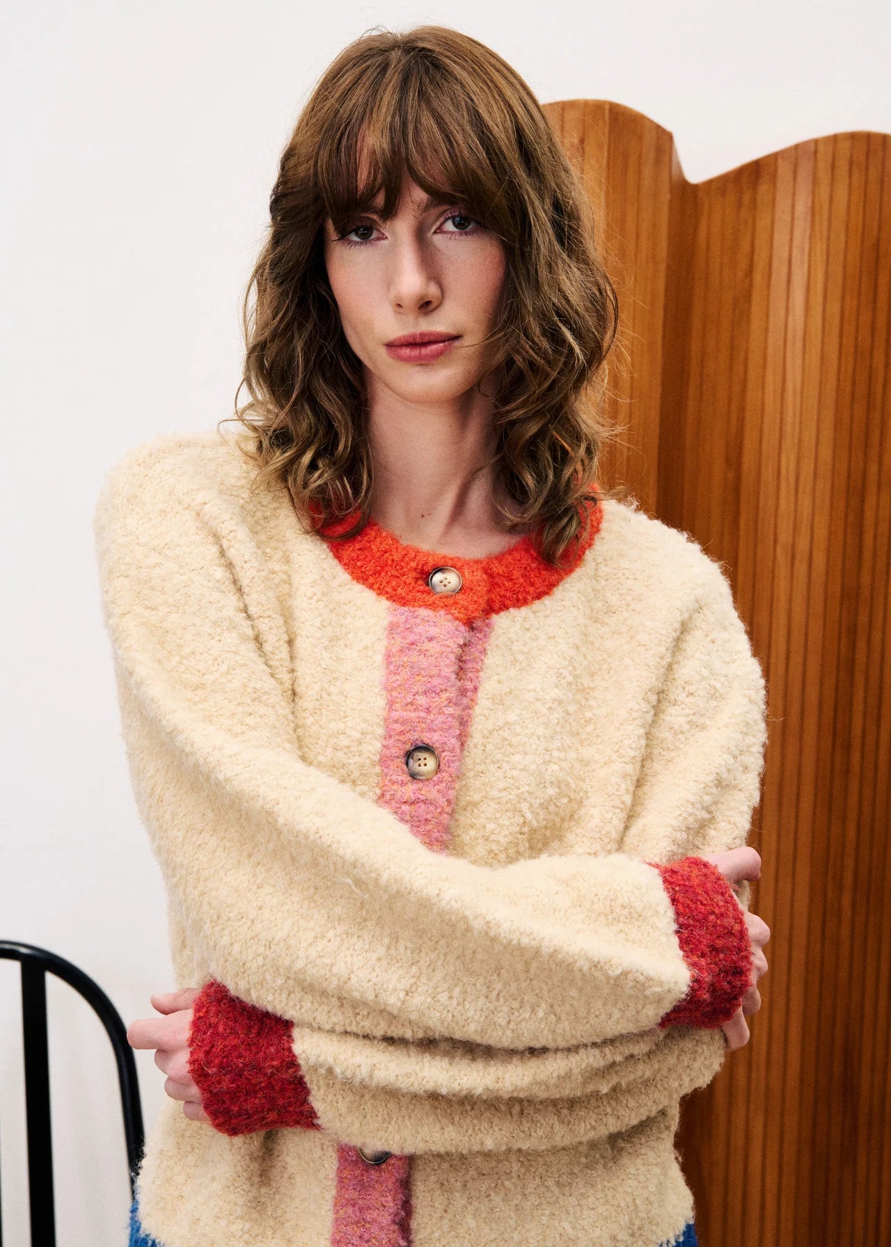 Woman wearing a cream cardigan with red accents in a room with wooden paneling.