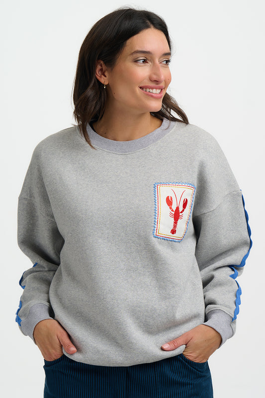 Woman wearing a gray sweatshirt with a lobster graphic on a white background