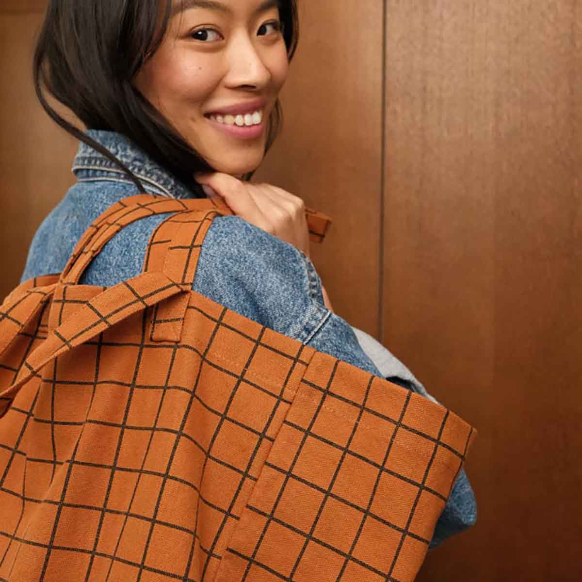 Woman wearing a brown grid-patterned apron over a denim jacket against a wooden background