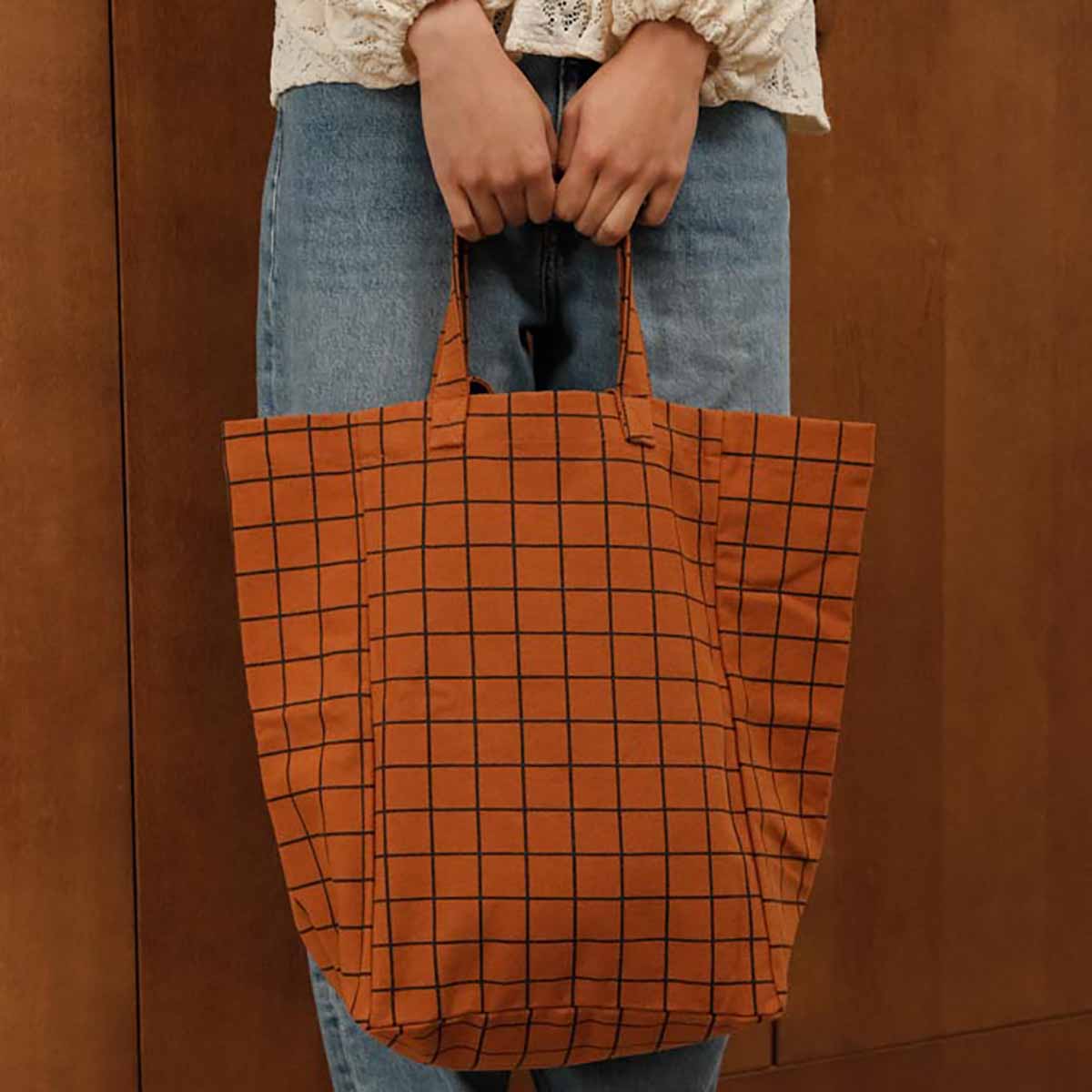 Person holding an orange tote bag with a grid pattern against a brown background