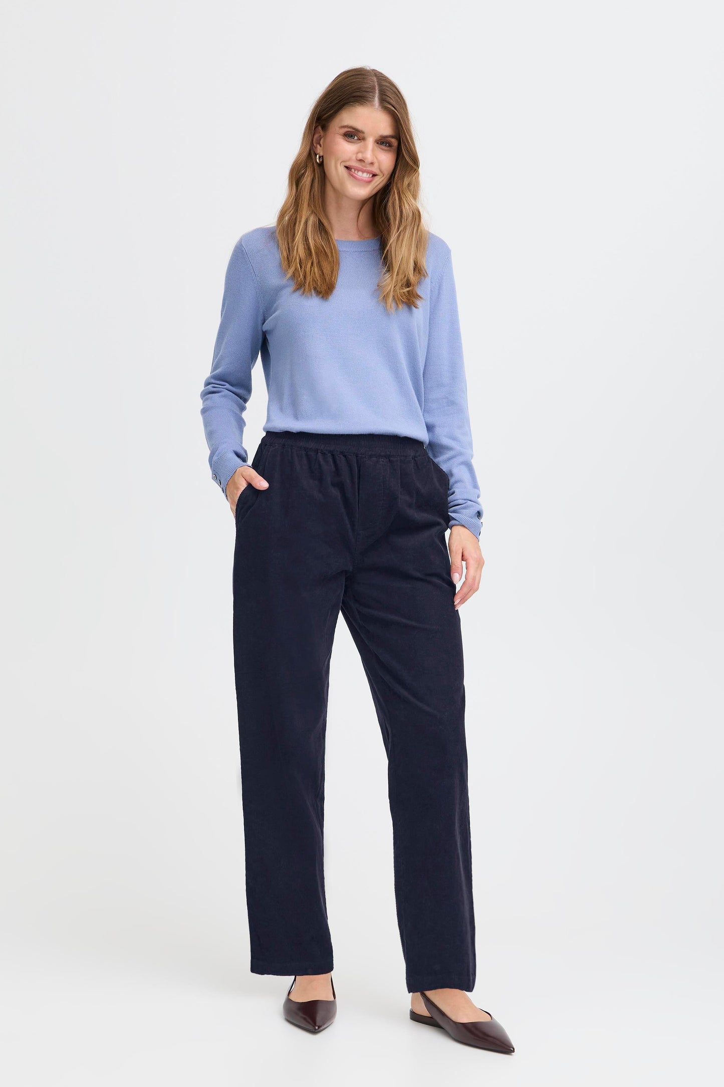 Woman wearing a light blue sweater and dark blue pants on a white background