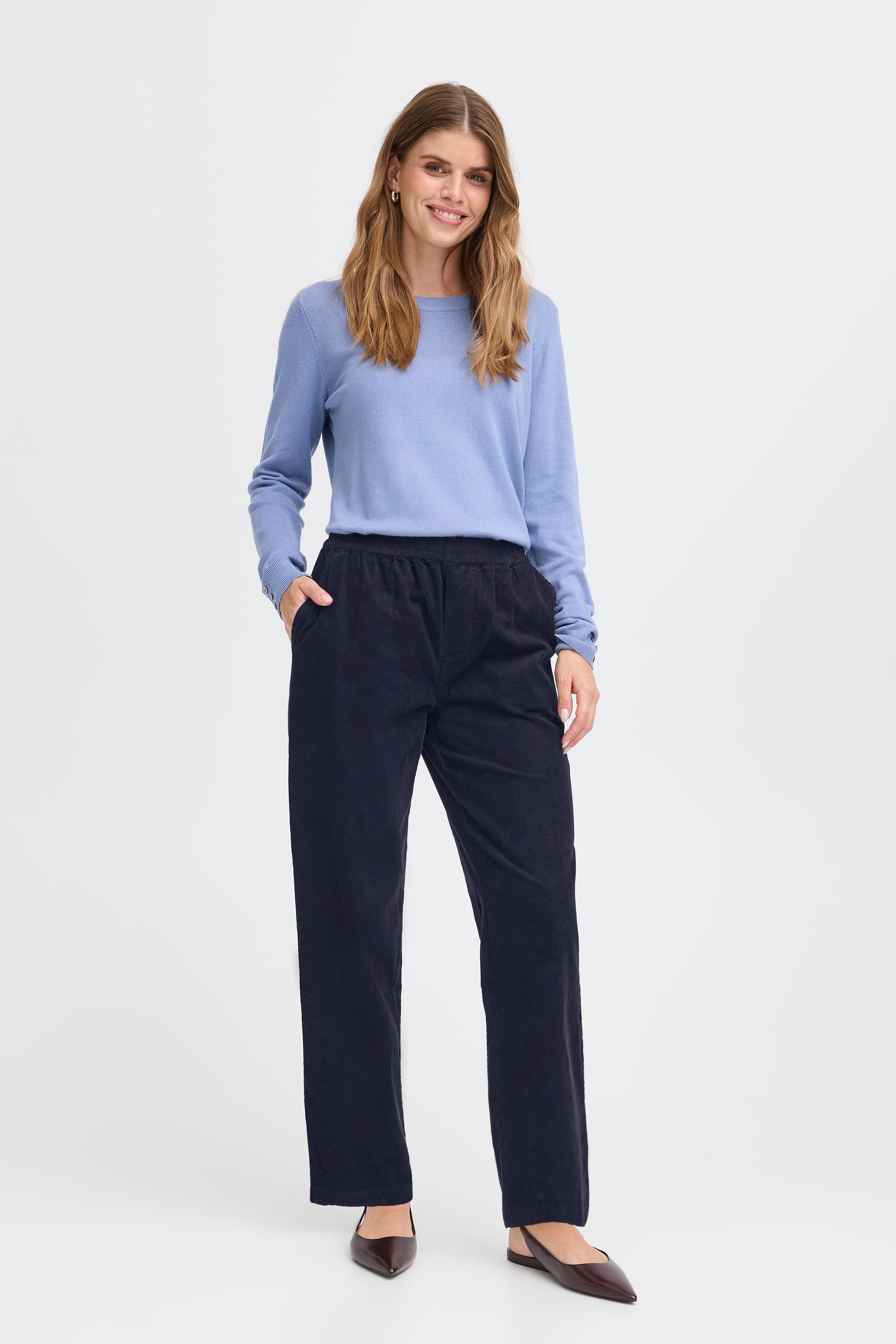 Woman wearing a light blue sweater and dark blue pants on a white background