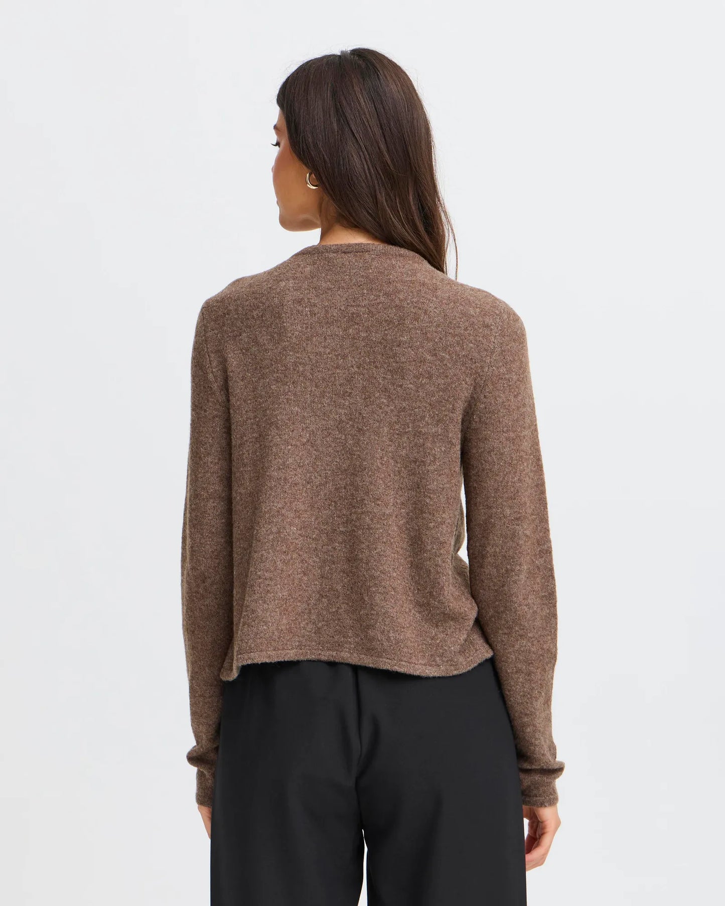 Person wearing a brown sweater and black pants on a light gray background