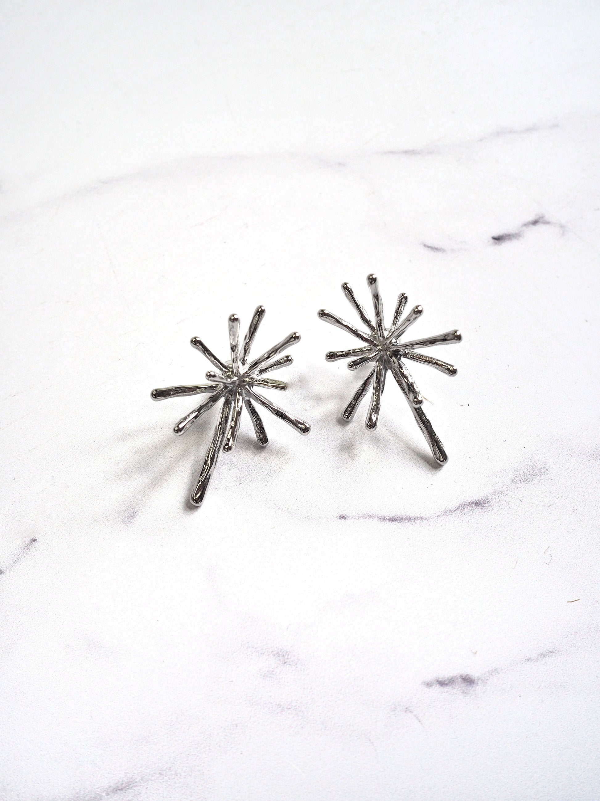 Pair of silver starburst earrings on a marble surface