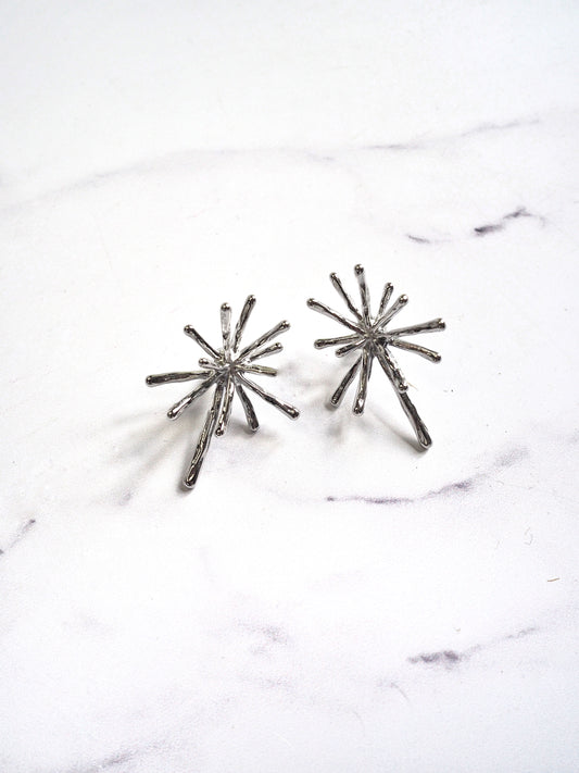 Pair of silver starburst earrings on a marble surface