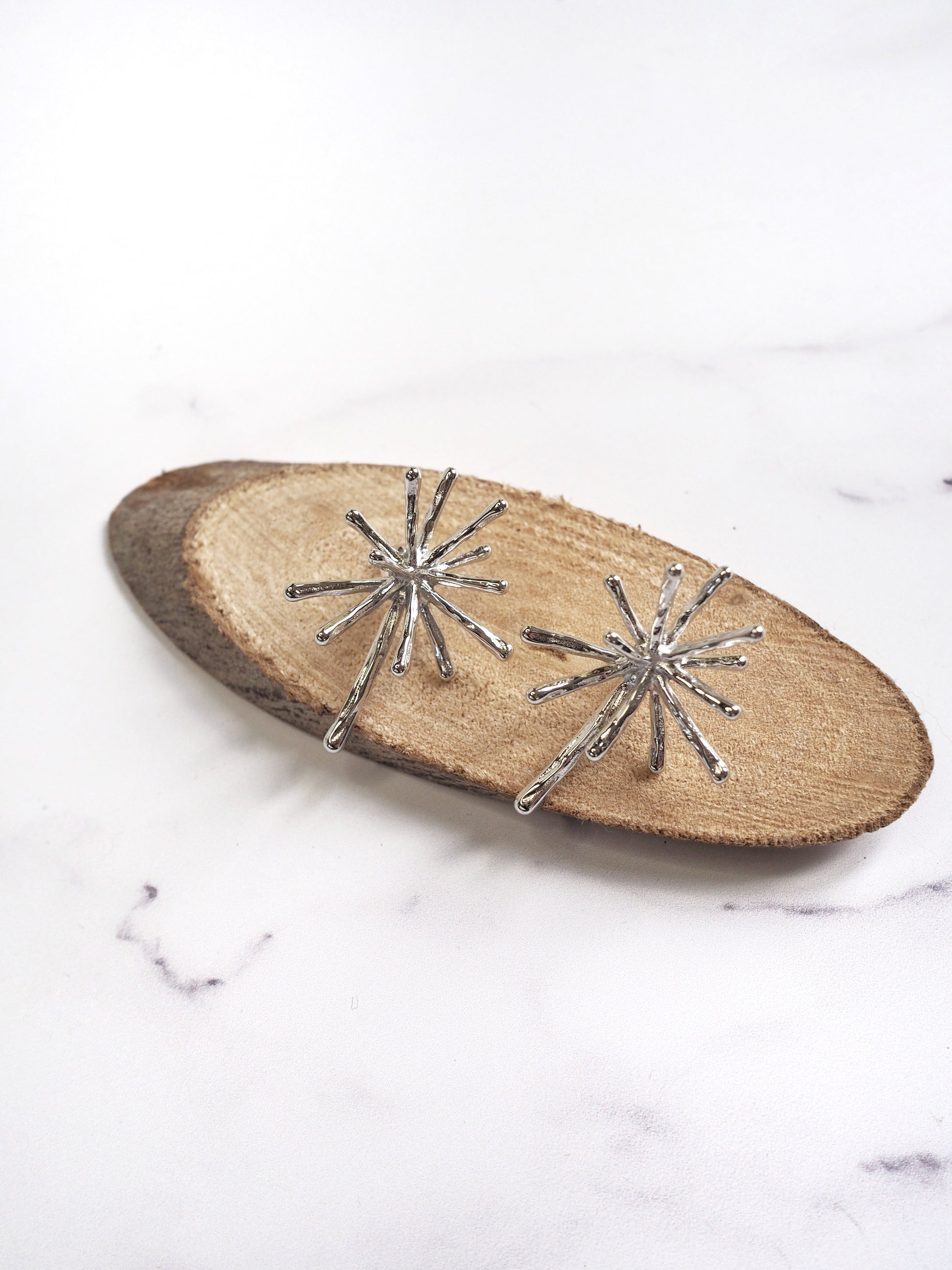 Silver starburst earrings on a wooden board with a marble background
