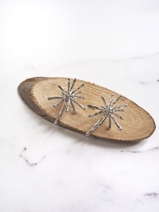 Silver starburst earrings on a wooden board with a marble background