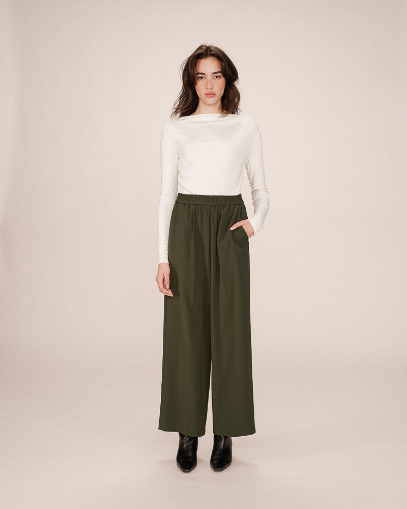 Woman wearing a white top and green wide-leg pants on a beige background
