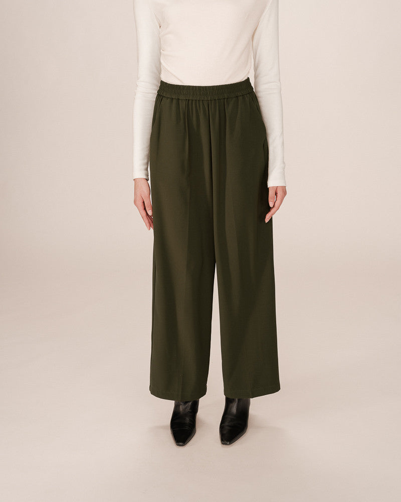 Person wearing olive green wide-leg pants and a white top on a beige background