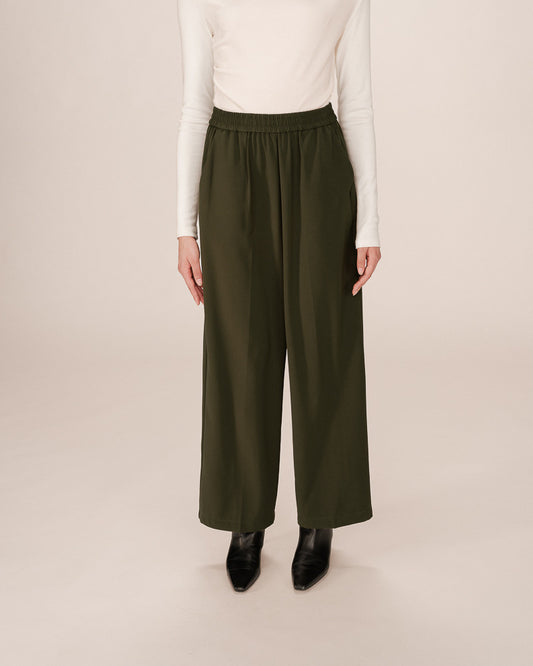 Person wearing olive green wide-leg pants and a white top on a beige background