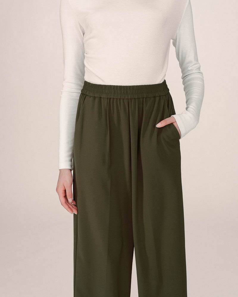 Person wearing olive green pants and a white long-sleeve shirt on a beige background