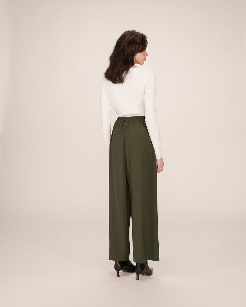 Woman wearing a white top and green wide-leg pants on a beige background