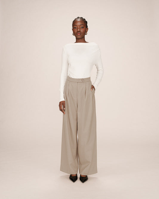 Woman wearing a white top and beige wide-leg pants on a plain background