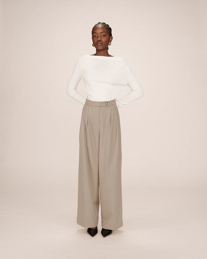 Person wearing a white long-sleeve top and beige wide-leg pants on a plain background