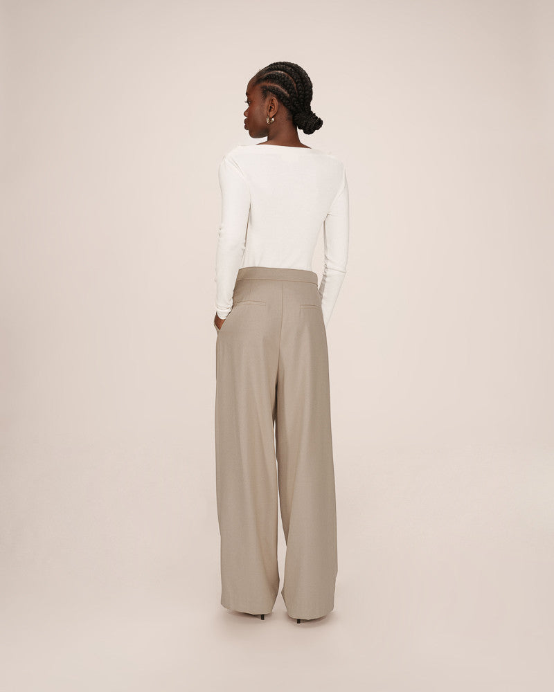 Woman wearing a white blouse and beige high-waisted pants on a plain background