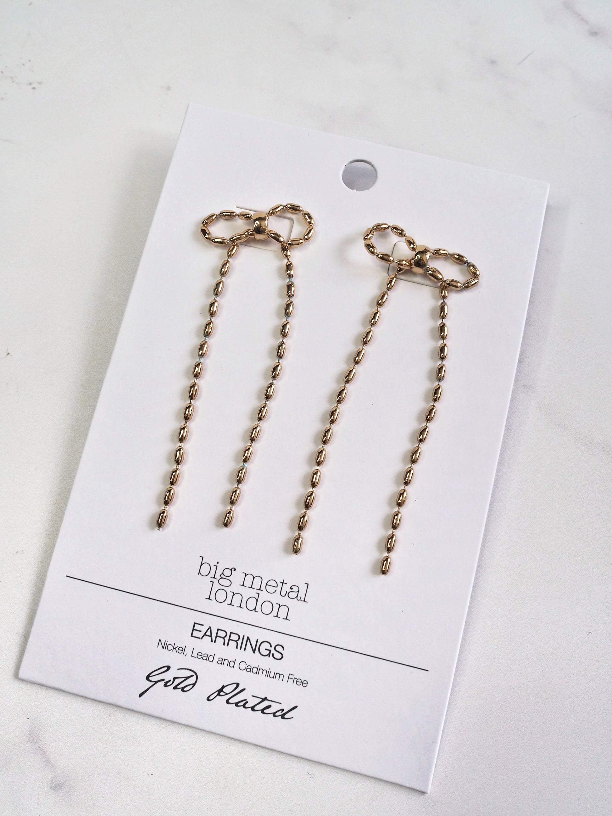Gold bow-shaped earrings on a 'big metal london' card with gold plating text.