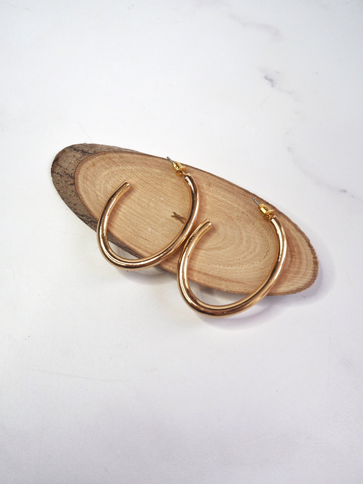 Gold hoop earrings on a wooden surface with a white background