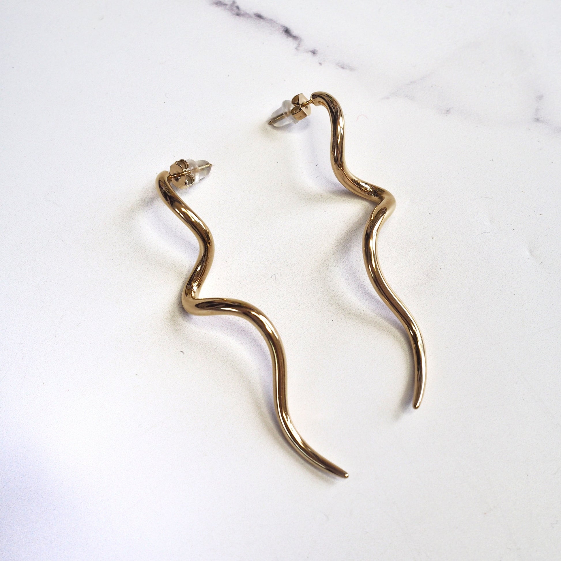 Gold snake-shaped earrings on a marble surface