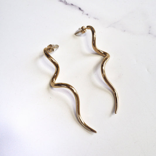 Gold snake-shaped earrings on a marble surface