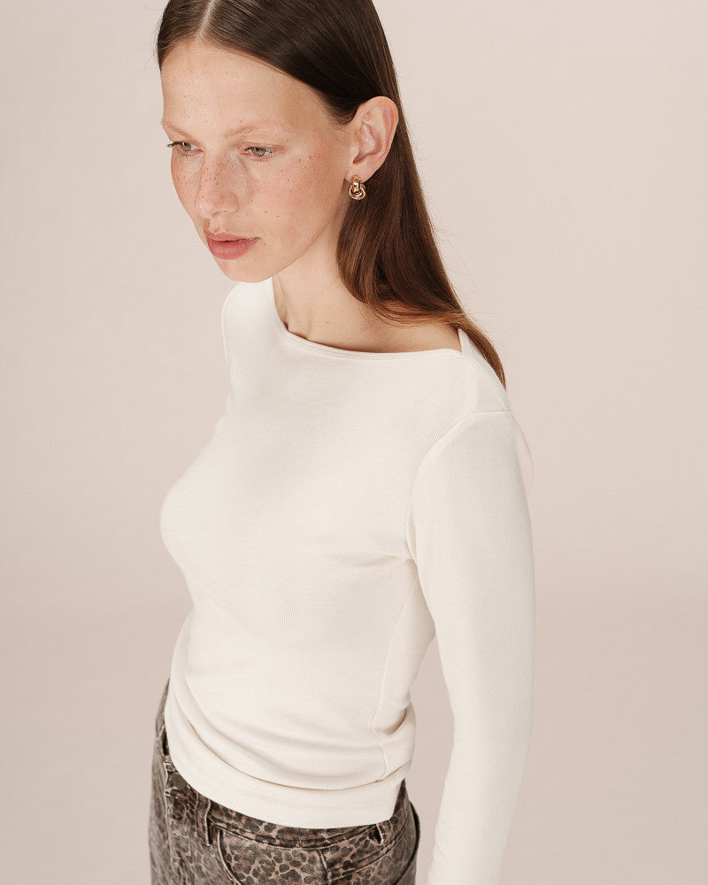 Woman wearing a white long-sleeve top against a plain background